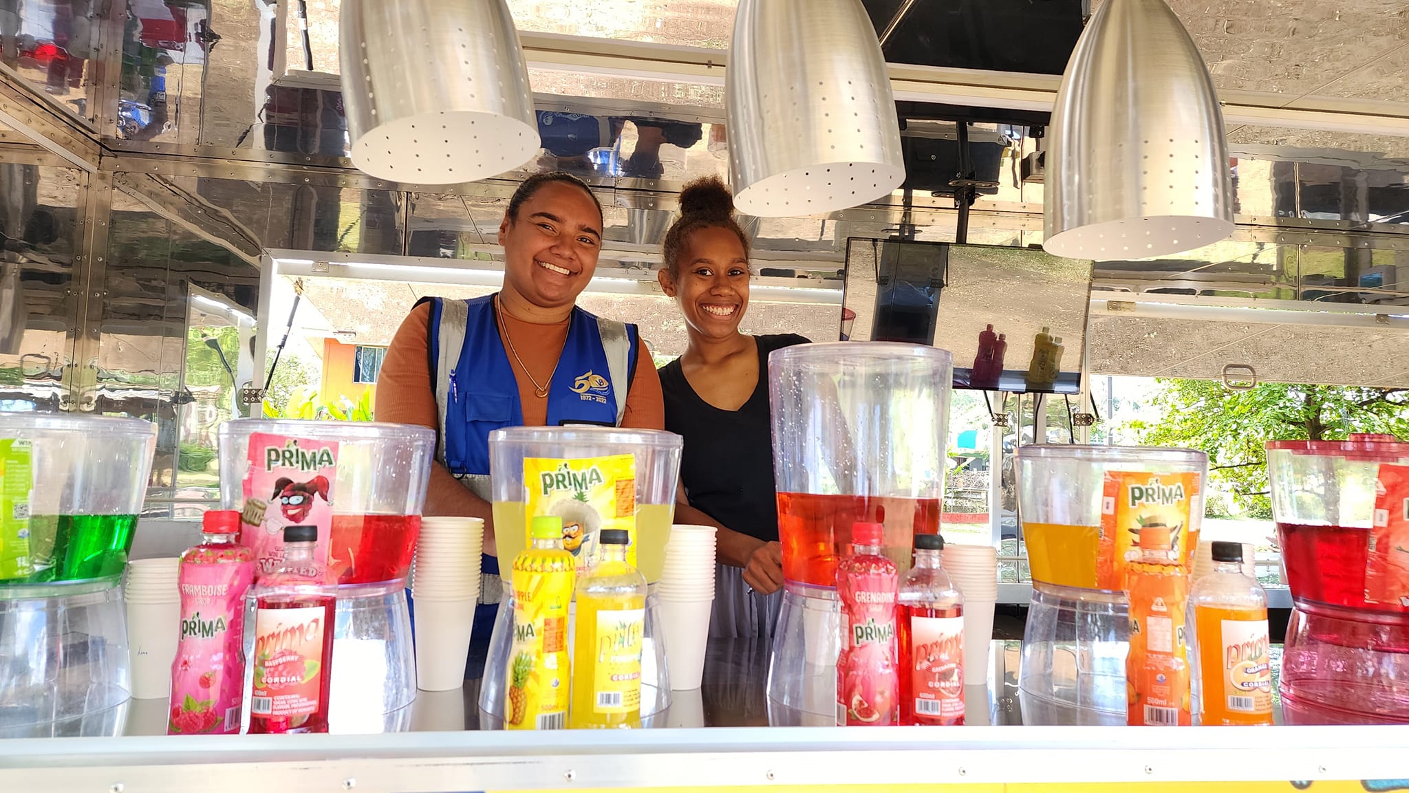 Smiling team serving colorful drinks from inside their custom trailer